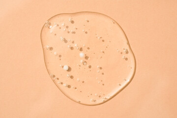 Drop of transparent cosmetic textured gel background with bubbles on beige glass. Copy space. Bath gel background