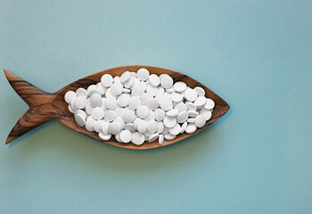 Calcium pills in a wooden dish in the form of a fish. Fish is rich in calcium. Color background....