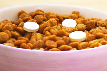 Cat food with three pills in a bowl on the floor. Vitamins for cats. Cat treatment. View of how a cat sees it
