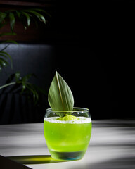 green small round cocktail with lemon and leaf in a bar