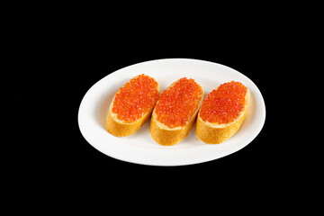 Naklejka na ściany i meble Red caviar on a piece of bread on a white plate isolated on a black background