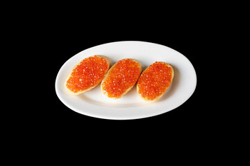 Red caviar on a piece of bread on a white plate isolated on a black background