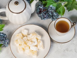 A teapot and a white mug on the table, flowers and traditional Turkish and Greek jelly candies in powdered sugar on a plate. confectionery in Arabic style..T The concept of recipes, 