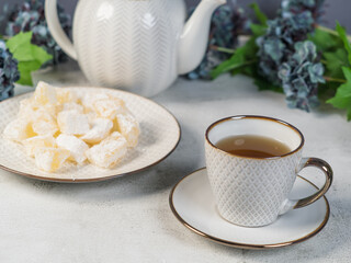 A teapot and a white mug on the table, flowers and traditional Turkish and Greek jelly candies in powdered sugar on a plate. confectionery in Arabic style..T The concept of recipes, 