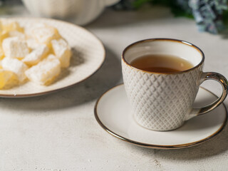 A teapot and a white mug on the table, flowers and traditional Turkish and Greek jelly candies in powdered sugar on a plate. confectionery in Arabic style..T The concept of recipes, 