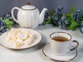 A teapot and a white mug on the table, flowers and traditional Turkish and Greek jelly candies in powdered sugar on a plate. confectionery in Arabic style..T The concept of recipes, 