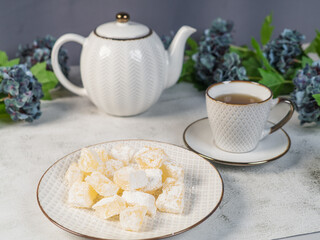 A teapot and a white mug on the table, flowers and traditional Turkish and Greek jelly candies in powdered sugar on a plate. confectionery in Arabic style..T The concept of recipes, 