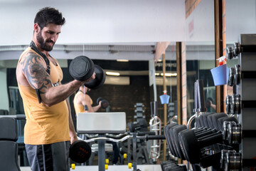 Homem com barba levantando peso na academia com espelho na frente horizontal