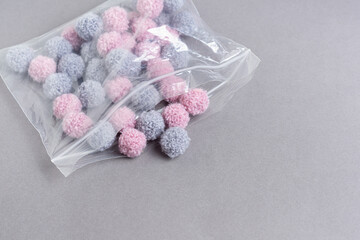 Fototapeta na wymiar Small fluffy pompoms for decorating in cellophane bag on gray background. Pompoms for creativity. Space for text 