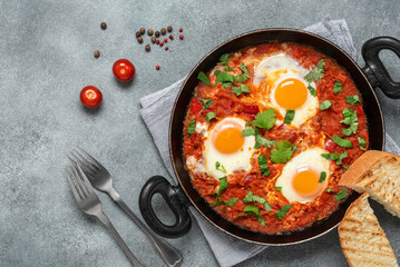 Shakshuka in a frying pan on a gray concrete rustic background. Poached eggs in a spicy tomato pepper sauce. Traditional Jewish scrambled eggs. Top view, flat lay,