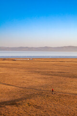Obraz premium L'immensité des rivages du lac Son Kul au Kirghizistan. Au loin, des yourtes et des montagnes. Une personne avec un chien