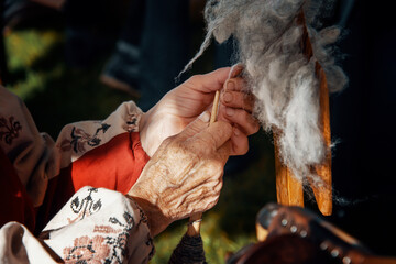 hands of an old woman. Hands spin yarn on an old spinning wheel. An old women's craft.