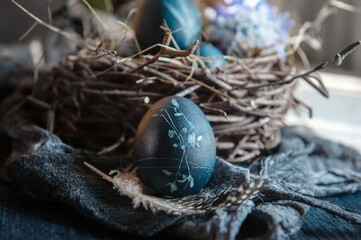 Blue Easter eggs in a round bird nest with processed hay on a blue background, monochrome Easter still life in a rustic style