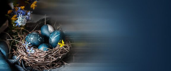 Blue Easter eggs in a round bird nest with processed hay on a blue background, monochrome Easter still life in a rustic style.