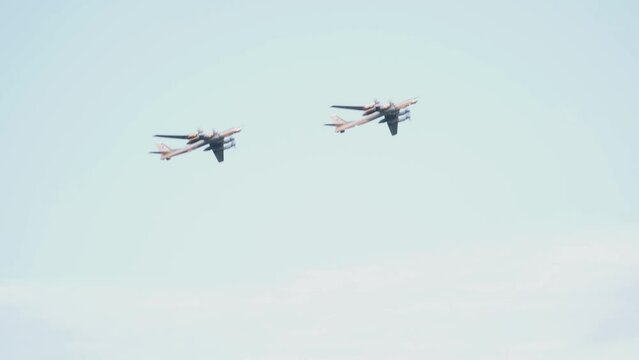 Two Russian military Tu-95 missile-carrying turboprop bombers fly in the blue sky. Close-up of propeller-driven aircraft.
