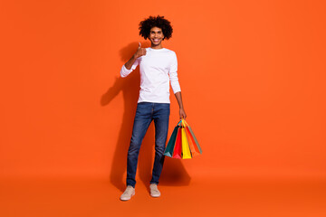 Photo of sweet cool guy wear white shirt jumping holding bargains thumb up empty space isolated orange color background