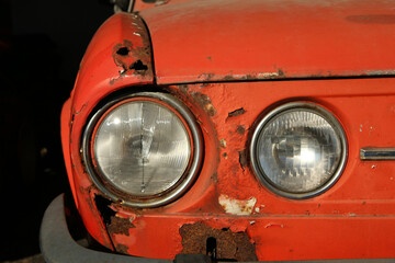 The detail of the front part of a neglected classic car. The metal bonnet and fender are rusted through and need renovation.