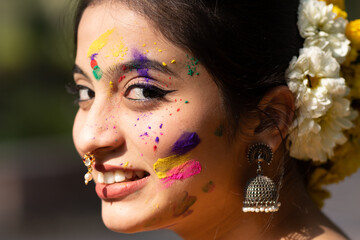 Portrait of a happy, beautiful and young smiling girl or woman in yellow saree with color on her...