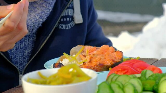 A man eats fish and rice outdoors using bamboo sticks