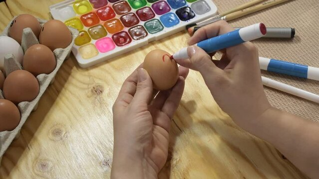 Easter decoration painted eggs with the image of a heart. Drawing a heart on an egg with a marker. Easter eggs drawing concept. Hands and egg clouse up.