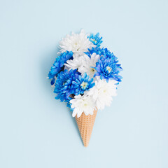 Blue and white flowers in ice cream cone on pastel blue background. Minimal concept. Flat lay.