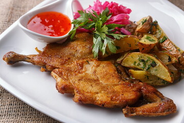 Fried chicken with potato wedges and spicy sauce on a white plate