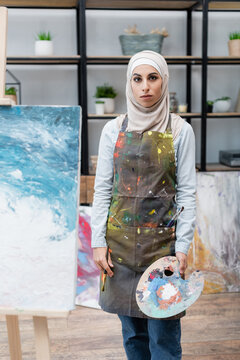 Arabian Woman With Pallet Looking At Camera Near Painting On Easel.