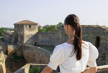 Fototapeta na wymiar Close-up woman in a white blouse background of the defensive stone walls of the old fortress. She looking on the medieval architecture with interest and delight. Travel tourist bastion Akkerman.