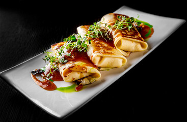 Thin pancakes crepe rolls with ground meat on plate on wooden table dark background
