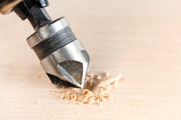 Countersink for deepening the self-tapping screw. A countersink drill makes a recess in a hole for a screw in a wooden board. - obrazy, fototapety, plakaty
