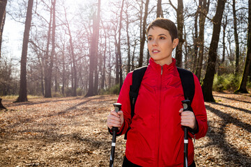 Young woman is making a hike in the woods. The woman has short hair, wears a red jacket and uses...