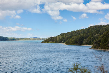 Lake between mountains and vegetation in argentine patagonia. Light blue sky with fluffy clouds.