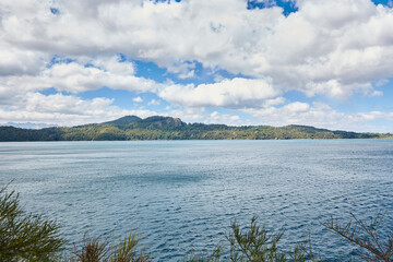 Lake between mountains and vegetation in argentine patagonia. Light blue sky with fluffy clouds.
