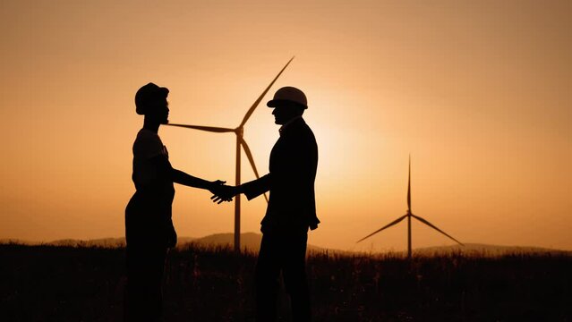 Silhouette man shaking hands with engineer with wind turbines on background. Two colleagues making deal about successful cooperation. Heartwarming uplifting picture of clean energy for the environment