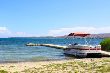 A catamaran with a red canopy against the backdrop of a lake and a pier with a sunbathing girl