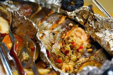 Baked fish in foil stuffed with rice and baked fruits spread around the edges. Shallow depth of field