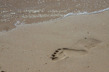Footprints of a man on the yellow beach sand from walking barefoot by the sea with water that washes away the footprints.