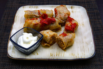 Traditional Caucasian dish Tolma or Dolma. Stuffed cabbage leaves with meat and rice, and a small glass container with sour cream on the same plate. Close-up