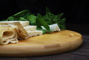 Village cheese, greens and Lavash on a serving board. Shallow depth of field