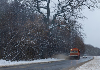 A large car with a plow clears the road from snow. Orange cargo special equipment is struggling...