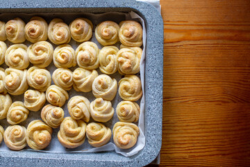 Baking buns in a metal gray baking sheet. Baking in the shape of a rose or snail. Baking snail. Close-up. Wooden table.