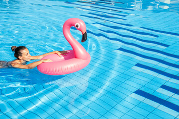 Summer time. Happy young sexy girl in bikini swimsuit with pink inflatable flamingo relaxing in blue pool water. Swimming pool water, having fun and enjoying travel vacation.