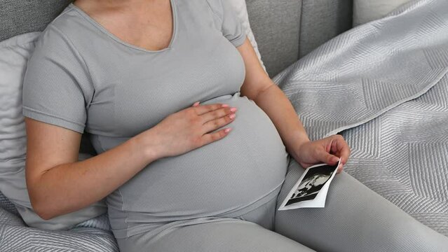 Pregnant woman cheking the sonogram sitting on teh bed