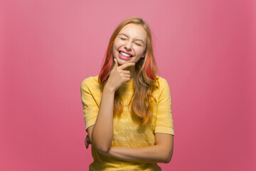 Joyful happy young girl laughs at joke, having fun, closed eyes on pink studio background. Positive emotions, optimism