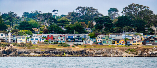 Houses in Pacific Grove, California (in Monterey County) overlook the rocky coastline, as viewed from a passing boat. - obrazy, fototapety, plakaty