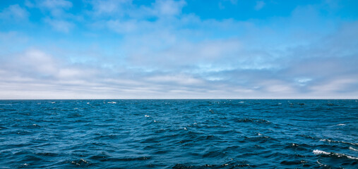 Colorful blue Pacific Ocean and partly cloudy sky background with copy space.