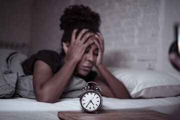 Attractive woman staring at alarm clock trying to sleep feeling stressed depressed and sleepless