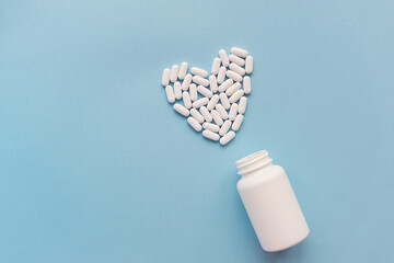 White pills in the shape of a heart and a white jar on a blue background. Pills for heart health....