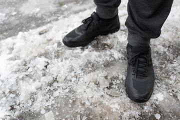 A man in winter waterproof sneakers stands on an icy road, shoes for winter walks. Walks in the open air.