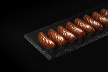 Sweets or candies on a black serving board. Assorted chocolate on a black isolated background